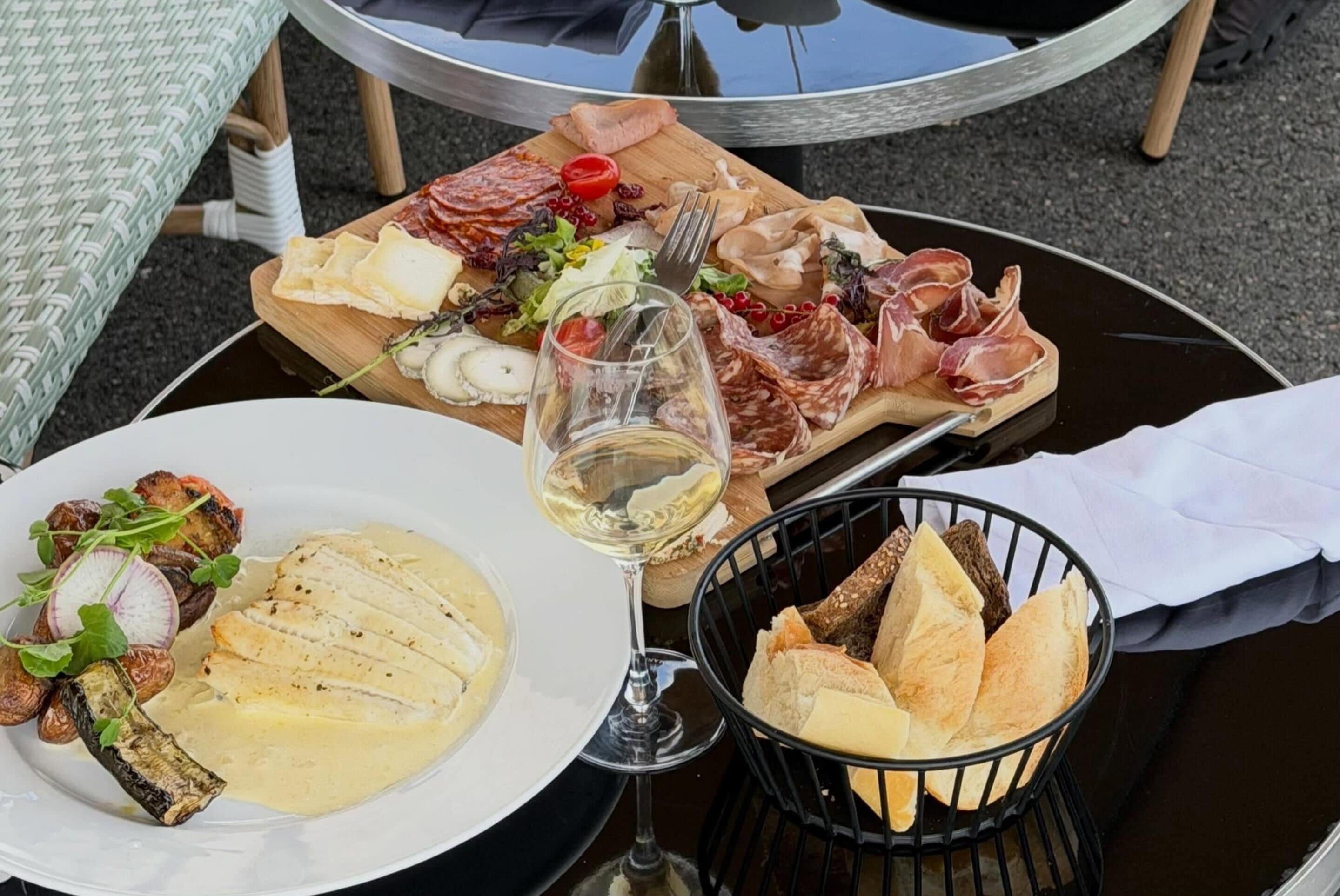 Ein Esstisch mit einem Teller Essen, einem Glas Weißwein und einem Korb Brot.