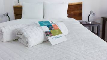 A neatly made bed with a folded white towel and a welcome card.