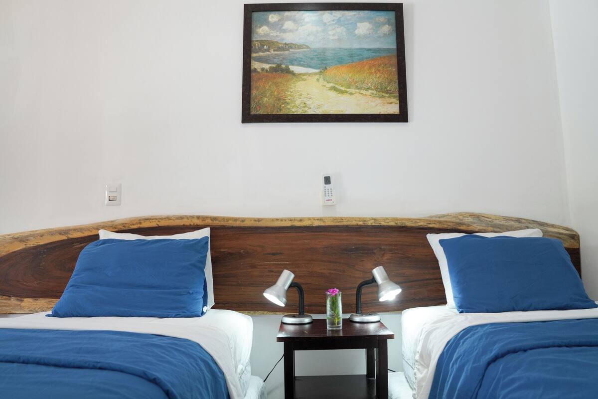 Hotelkamer met twee bedden, een houten hoofdbord, nachtkastjes met lampen en een schilderij aan de muur.