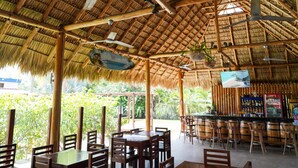 A restaurant with a thatched roof, wooden furniture, and a bar area. - Hotel Ingigante (Tola)