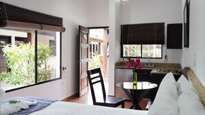 A hotel room with a bed, a small dining table with chairs, a kitchen area, and a view of greenery outside. - Hotel Ingigante (Tola)