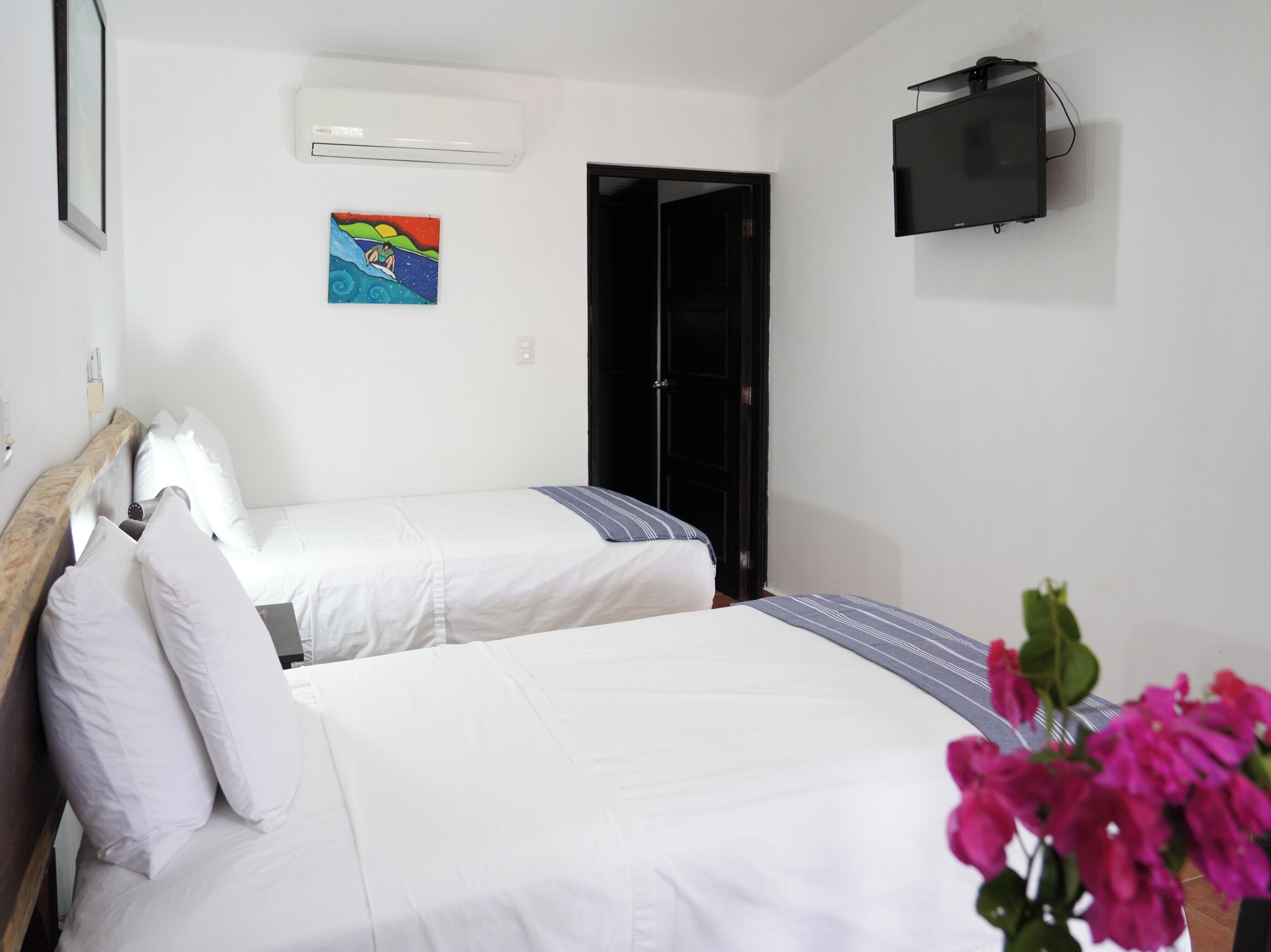 A hotel room with two beds, a TV mounted on the wall, and a colorful painting on the wall.