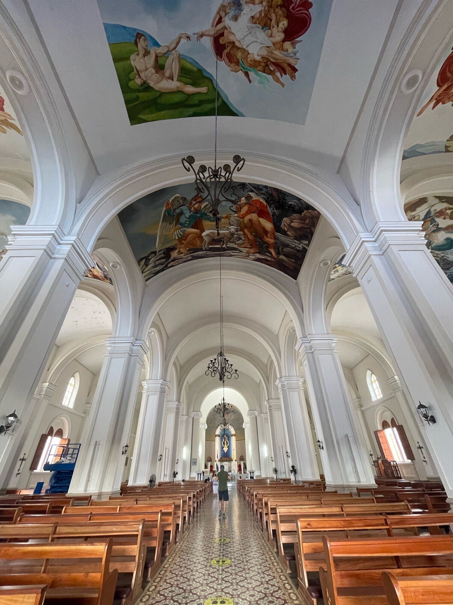 Interior de una iglesia con techos altos, columnas arqueadas, bancos de madera y un pasillo central que conduce al altar.