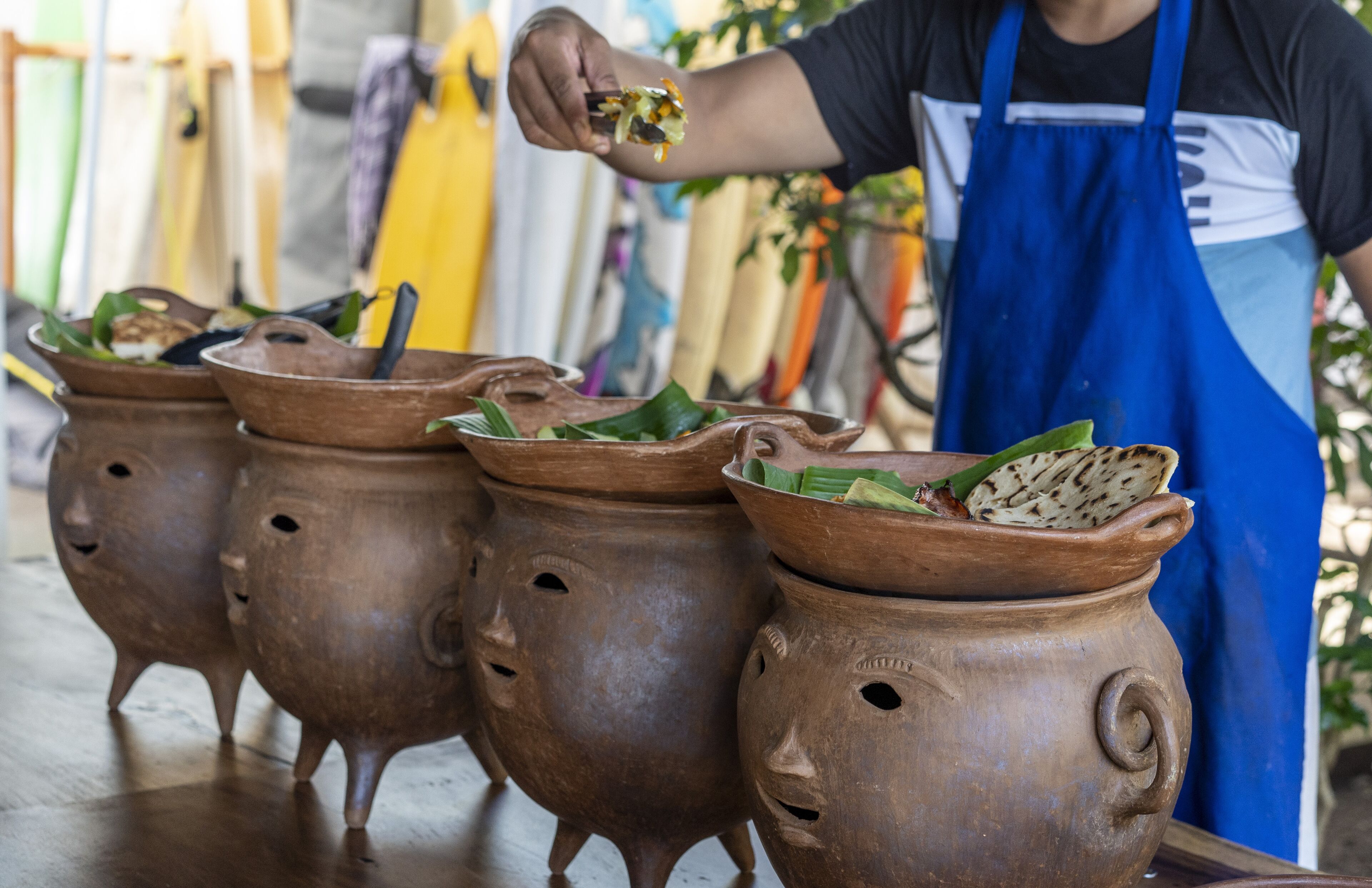 Una persona con delantal azul preparando comida en una olla de barro.