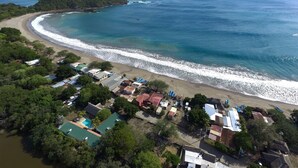 An aerial view of a coastal area with a beach, houses, and a small island. - Hotel Ingigante (Tola)