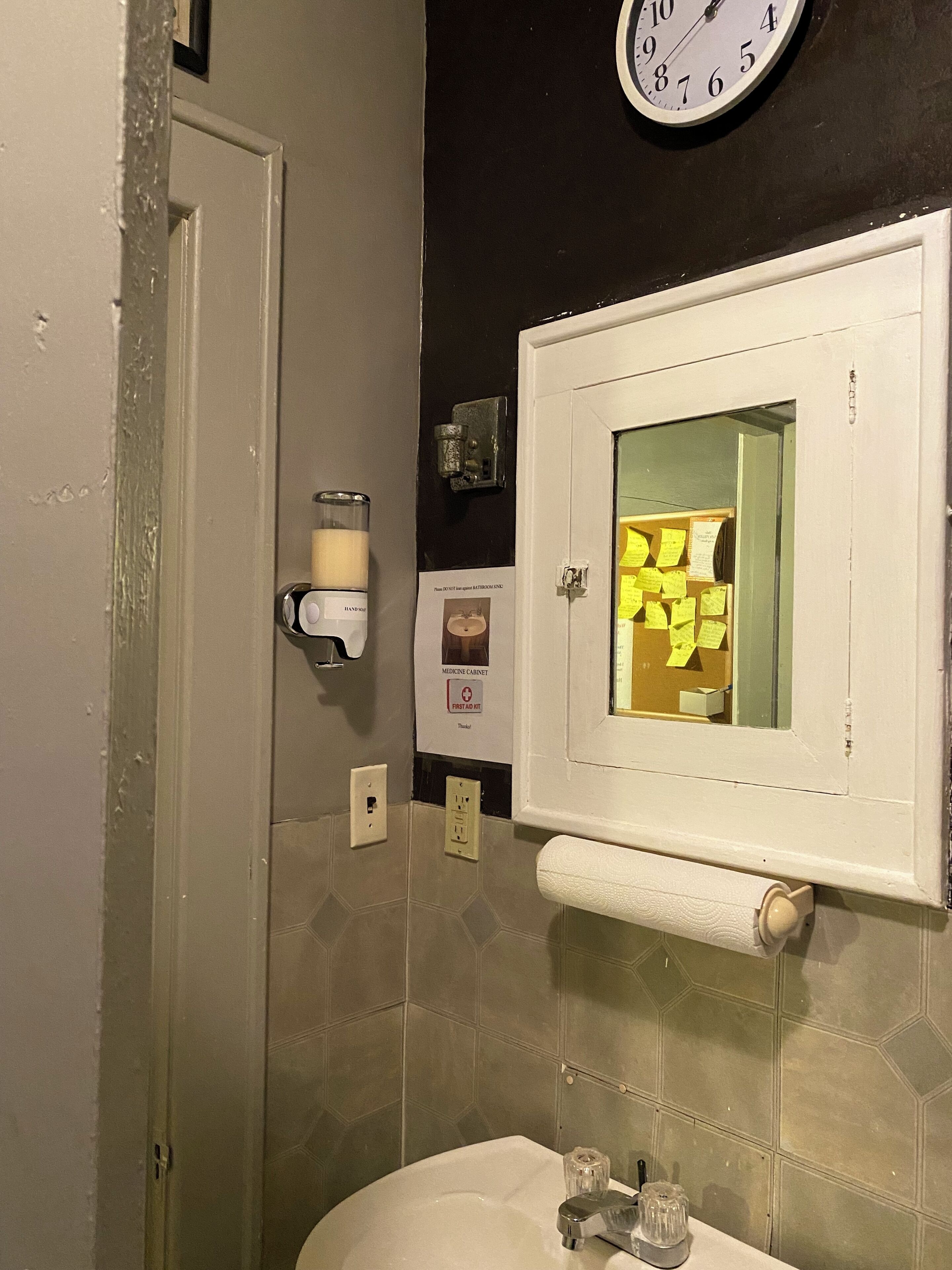 Un baño con lavamanos, espejo, reloj y mueble de medicinas.