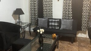 Ein Wohnzimmer mit einer Couch, einem Couchtisch mit Blumen und einer Lampe, ergänzt durch bunte Vorhänge.