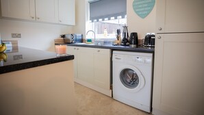 A compact kitchen with white cabinets, a built-in washing machine, a coffee maker, and a window with a view. - 5star Serviced Homes- Free Wifi & Parking, Office (Sunderland)