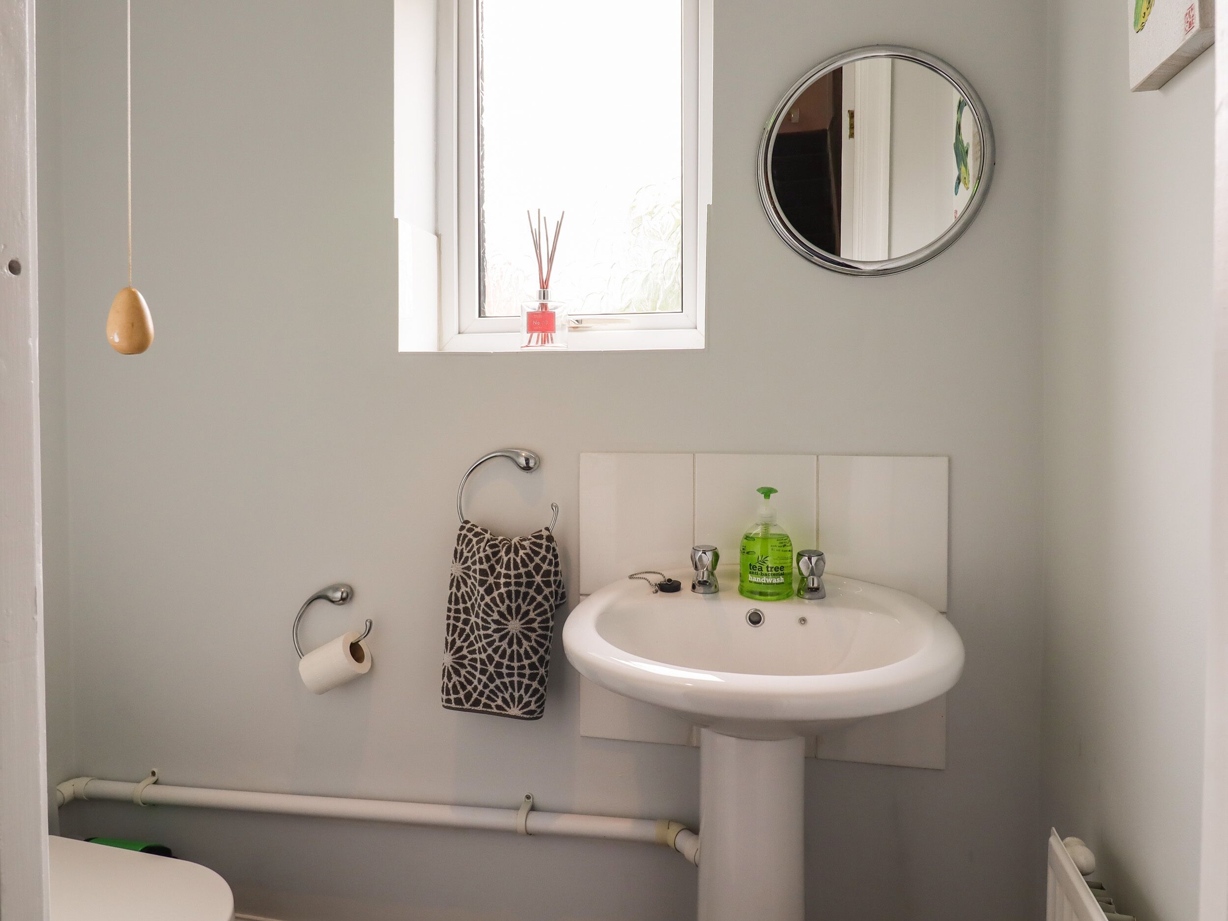 A bathroom with a white sink, a mirror, a window, a toilet, and a hanging towel rack.
