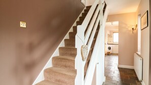A staircase with carpeted steps and white railings, leading to a room with a tiled floor and a visible washing machine. - 23 Brandeston Close (Sudbury)