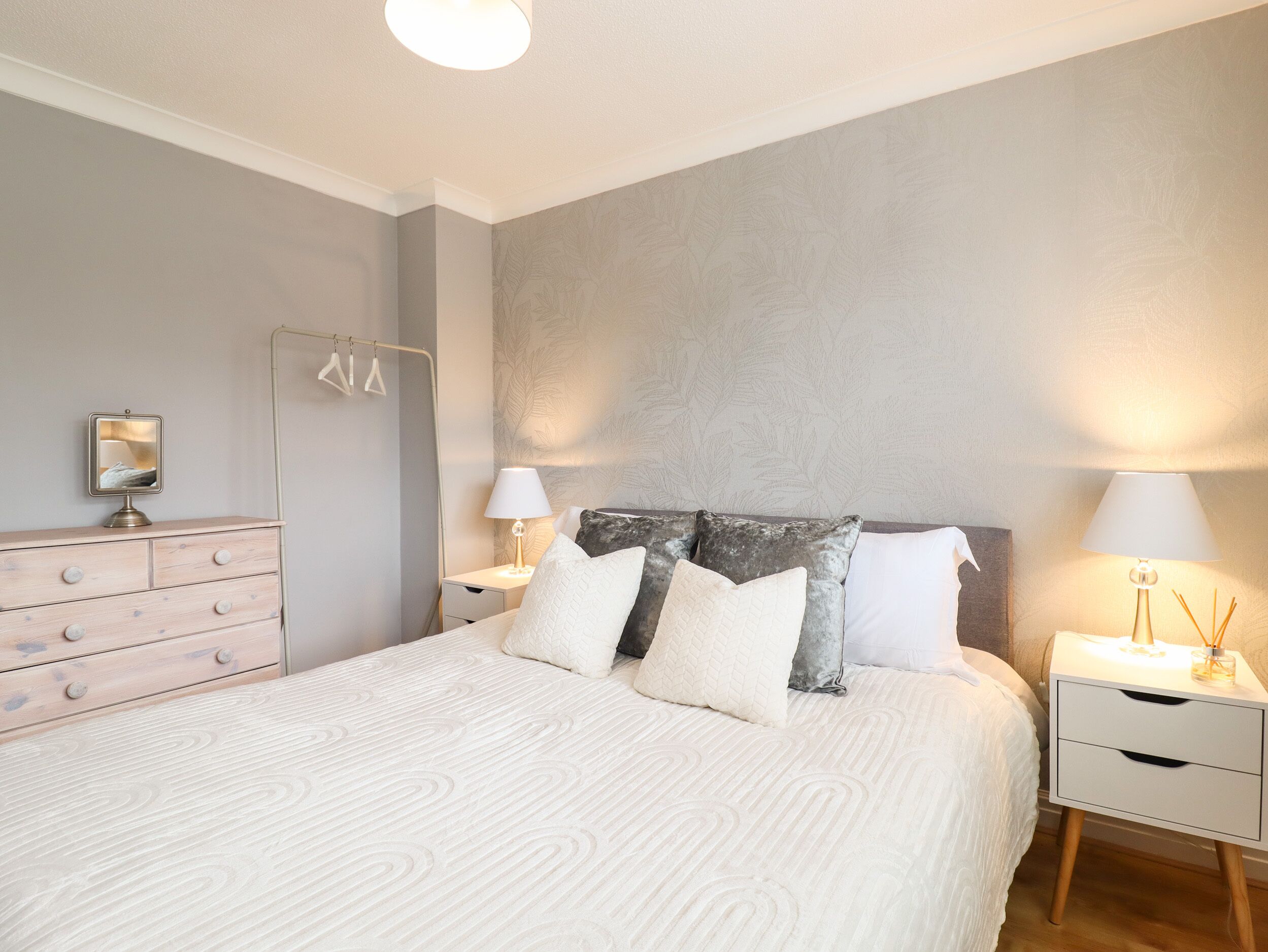 A neatly arranged bedroom with a bed, bedside tables, a dresser, and a mirror.