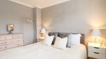 A neatly arranged bedroom with a bed, bedside tables, a dresser, and a mirror.