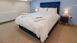 A bedroom with a bed, two bedside tables, a skylight, and a radiator. - 1 Bears Court Little Rissington (Cheltenham)