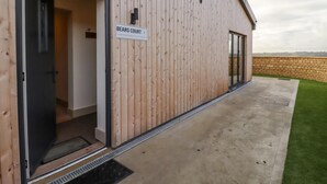 A modern building with a wooden exterior, a sign reading "BEARS COURT 4", and a concrete patio with a grassy area. - 1 Bears Court Little Rissington (Cheltenham)