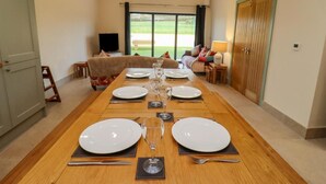 A dining room with a long wooden table set for a meal, a sofa, and a view of the outdoors. - 1 Bears Court Little Rissington (Cheltenham)