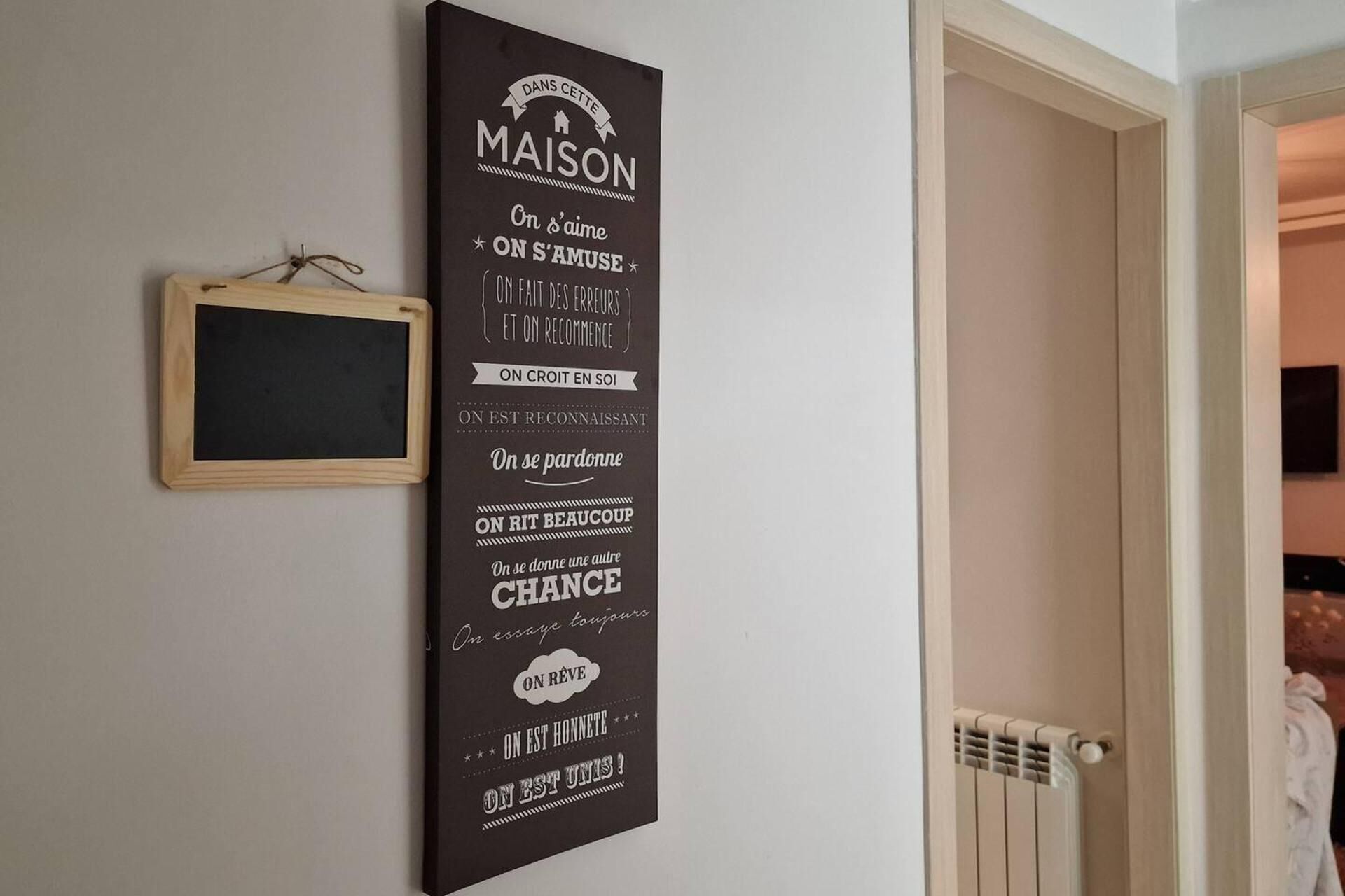 Ein vertikales Schild mit Schrift auf einer Wand, eine kleine Tafel in Holzrahmen und ein Heizkörper.