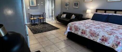 A bedroom with a bed, a desk, a chair, a sofa, and a door leading to another room.