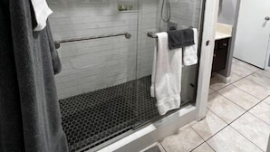 Un baño moderno con ducha de vidrio, toallero y piso de baldosas.