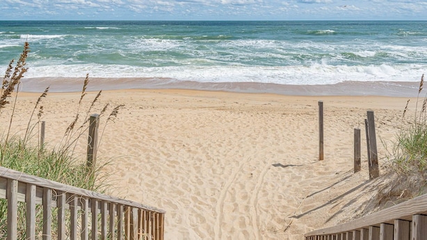 Una playa con un paseo de madera que conduce a la orilla, arena y olas del océano.