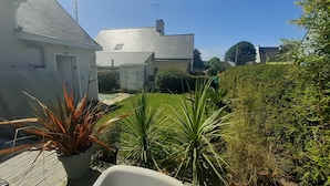 A residential garden with a white house, a paved patio, and various plants. - Maison au Calme Près des Plages (Concarneau)