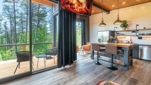 Una cocina moderna con una televisión grande que muestra un fuego, suelo de madera y un balcón con mobiliario de exterior.