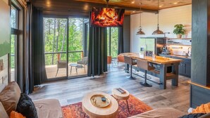 Una sala de estar moderna con un televisor grande, muebles de madera y vistas al exterior.