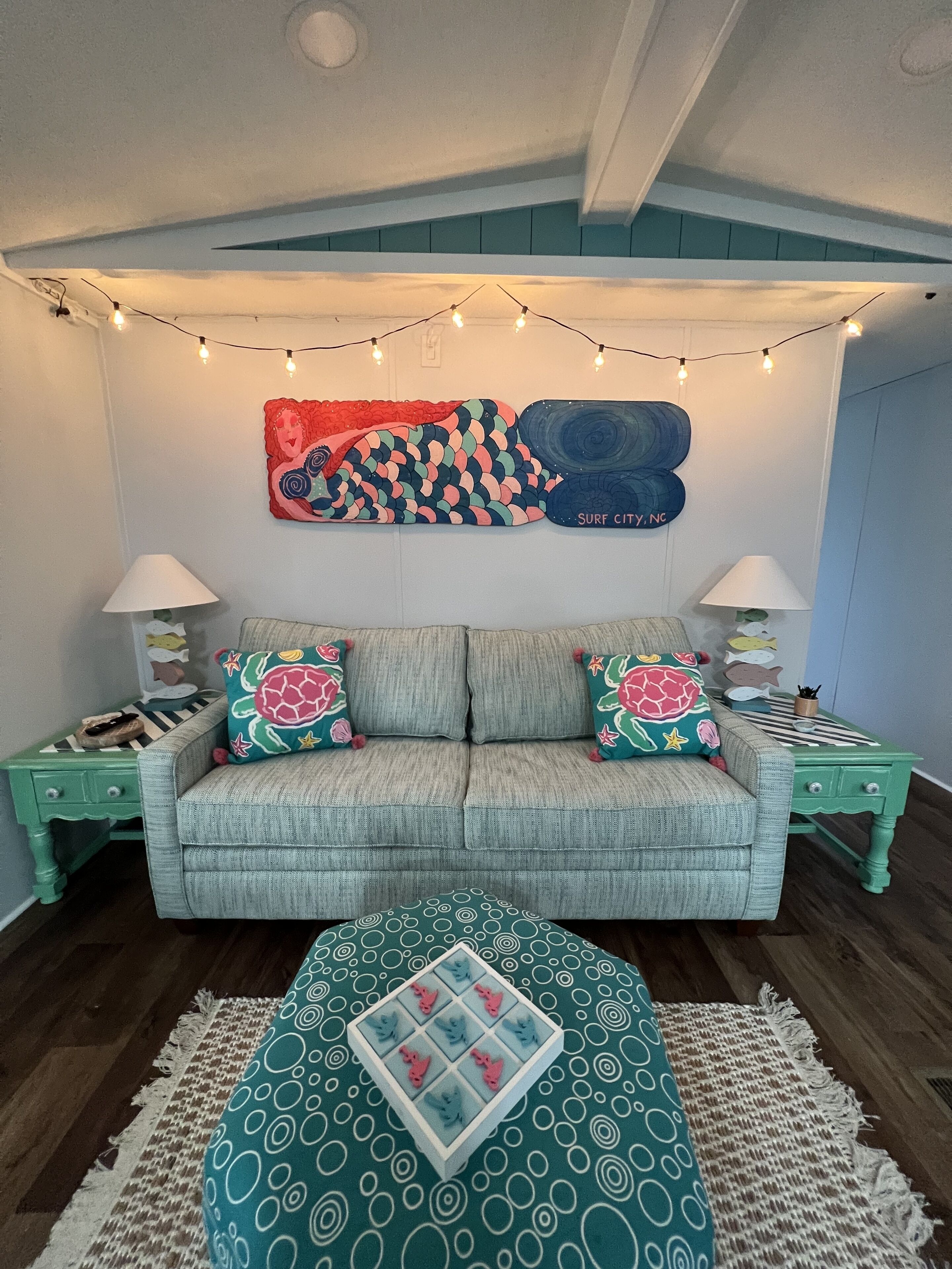 A cozy living room with a sofa, two side tables, a patterned rug, and string lights.