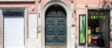 A building facade with a green double door, a closed white door, and a shop with a green sign.