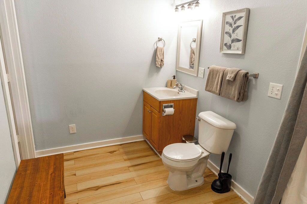 Een badkamer met een houten wastafelmeubel, toilet, wastafel, spiegel en handdoekrek.