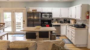 A compact kitchen with white cabinets, a stainless steel refrigerator, a microwave, and a coffee maker. There is a dining table with two chairs and a small rug on the floor. - 4 Bed | Hot Tub | Close to IU | Pet Friendly (Bloomington)