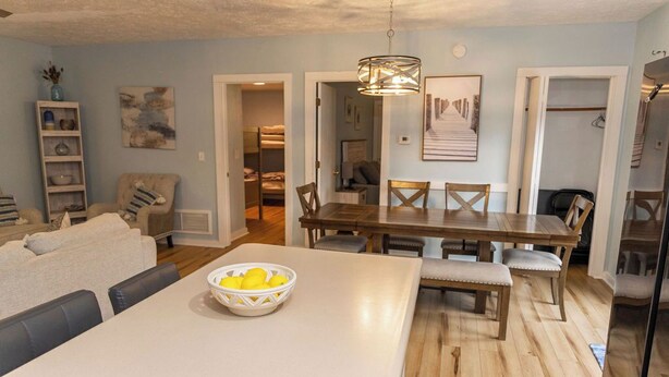 A modern living room with a white sofa, a dining table with wooden chairs, and a white bowl on the table. - 4 Bed | Hot Tub | Close to IU | Pet Friendly (Bloomington)