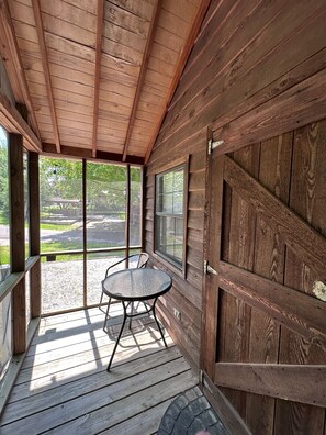 A wooden porch with a glass door and windows, a round table, and a bench. - Homey Cabin in Bloomington (Bloomington)