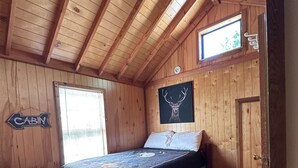 Ein blockhaushaftes Zimmer mit einem Bett, einem Fenster, einem Holztisch und einer Tür.