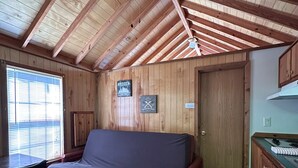 Ein kleiner Raum mit Holzbalkendecke, Deckenventilator, Sofa, Esstisch mit Stühlen und einer Küchenzeile.