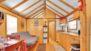 Een klein, houten huisje met een kitchenette, een eethoek en een slaapgedeelte.