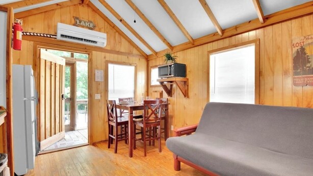 Een chalet met houten inrichting, een eethoek met tafel en stoelen, een grijze bank en een tv aan de wand.