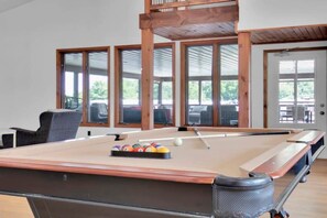 Relax in a spacious room with a pool table, comfortable seating, and large windows offering a view of the outdoors.