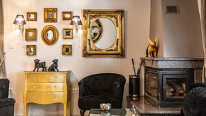 Un salon avec une cheminée, un fauteuil noir, un meuble en bois, ainsi que des miroirs et des cadres accrochés au mur.