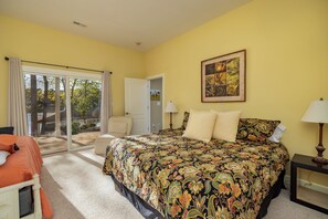 A bedroom with a large bed, a chair, a lamp, and a view through a sliding glass door.
