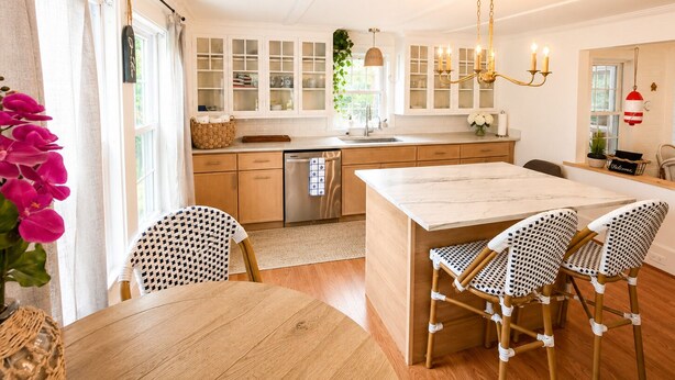 Een moderne keuken met witte kasten, een centraal eiland en een eetgedeelte met rieten stoelen.