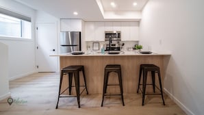 Une cuisine moderne avec des meubles blancs, des appareils en acier inoxydable et un îlot central doté de tabourets.