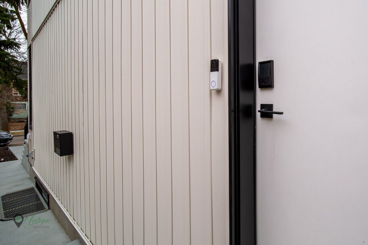 A modern building exterior with a beige siding, a black door, and a security camera.
