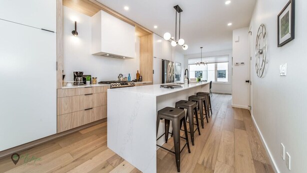 A modern kitchen with a central island, bar stools, and a view to the living area. - Full Home w/ Separate BSMT | Sleeps 12| King Beds (Edmonton)