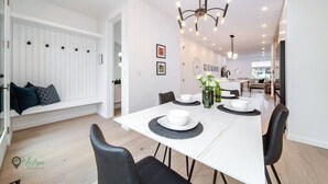 A modern dining area with a white table, black chairs, and a chandelier. - Full Home w/ Separate BSMT | Sleeps 12| King Beds (Edmonton)