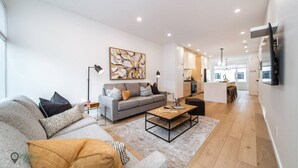 A modern living room with a grey sofa, a coffee table, and a painting on the wall. - Full Home w/ Separate BSMT | Sleeps 12| King Beds (Edmonton)