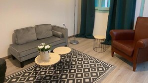 A modern living room with a grey sofa, a brown leather armchair, a small round table with a white vase, and a patterned rug.