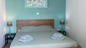 A bedroom with a wooden bed, two bedside tables with lamps, a floral picture on the wall, and a ceiling light fixture.