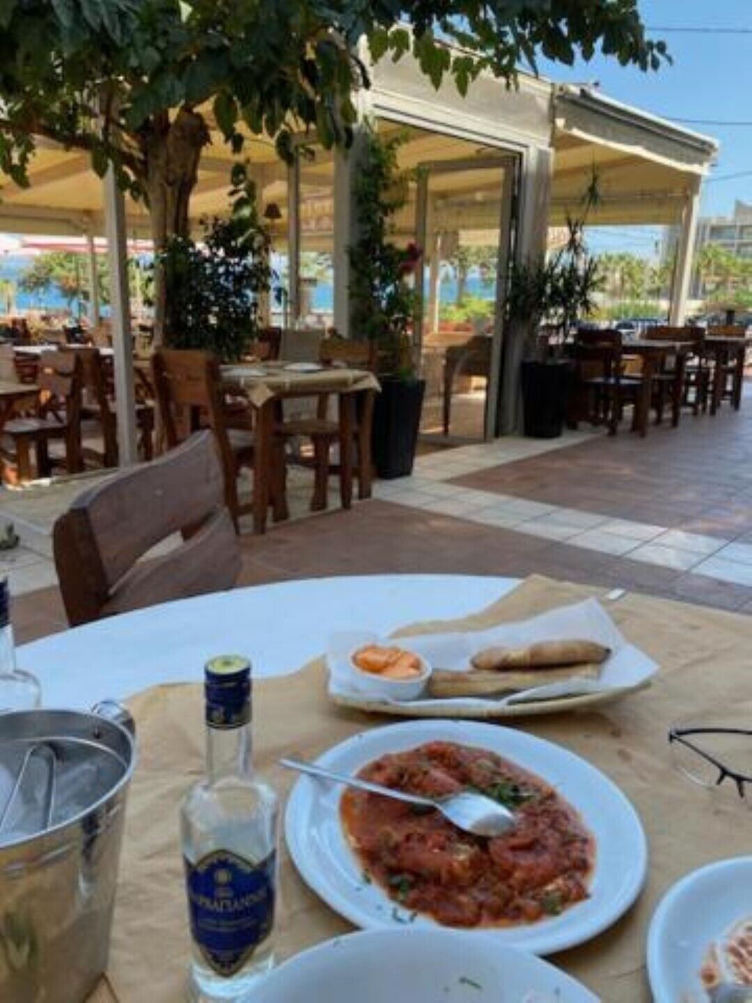 An outdoor dining area with tables, chairs, and a variety of dishes including pasta and a bottle of liquor.