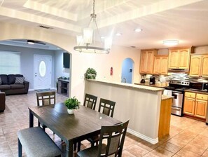 A modern kitchen with wooden cabinets, a central island, and a dining area with a dark wooden table and chairs. - Charming 4beds/2bath Entire Home (Eagle Pass)