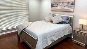 Una camera da letto con un letto, un comodino, una lampada, un quadro e una finestra con persiane.